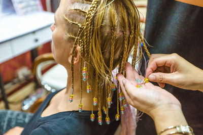 Cropped hands of beautician holding beads by woman sitting at salon