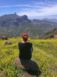 Rear view of woman sitting on rock at mountain