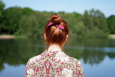 Back view of woman with red hair bun looking at lake