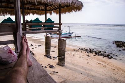 Low section of man resting in hut at beach against sky