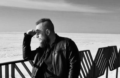 Rear view of man smoking at beach against sky