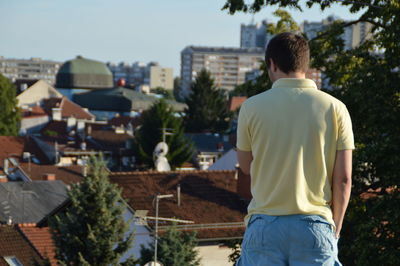 Rear view of man standing by buildings in city against clear sky