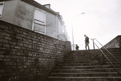 Low angle view of father and son standing on steps against clear sky