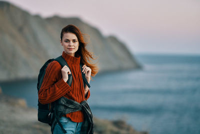 Portrait of smiling young woman standing against sea