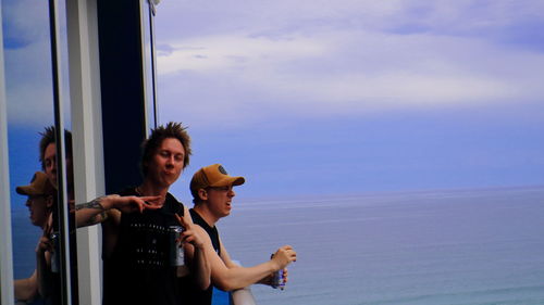 Two mates enjoying refreshing beers on hotel balcony against blue sky in gold coast australia