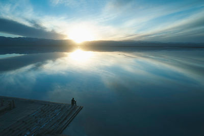 Silhouette mature man sitting on pier over sea against sky during sunset