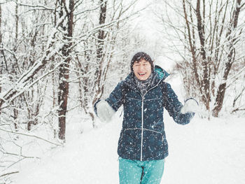 Smiling woman plays with snow. fun in snowy winter forest. woman laughs as she walks through wood.