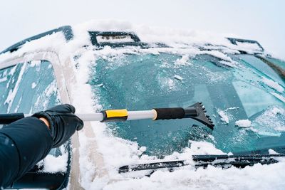 Man clearing snow off the windshield of the car in a winter day