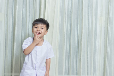 Cheerful boy standing against curtain at home