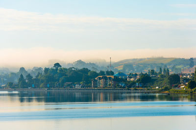 Scenic view of lake by buildings against sky during sunset