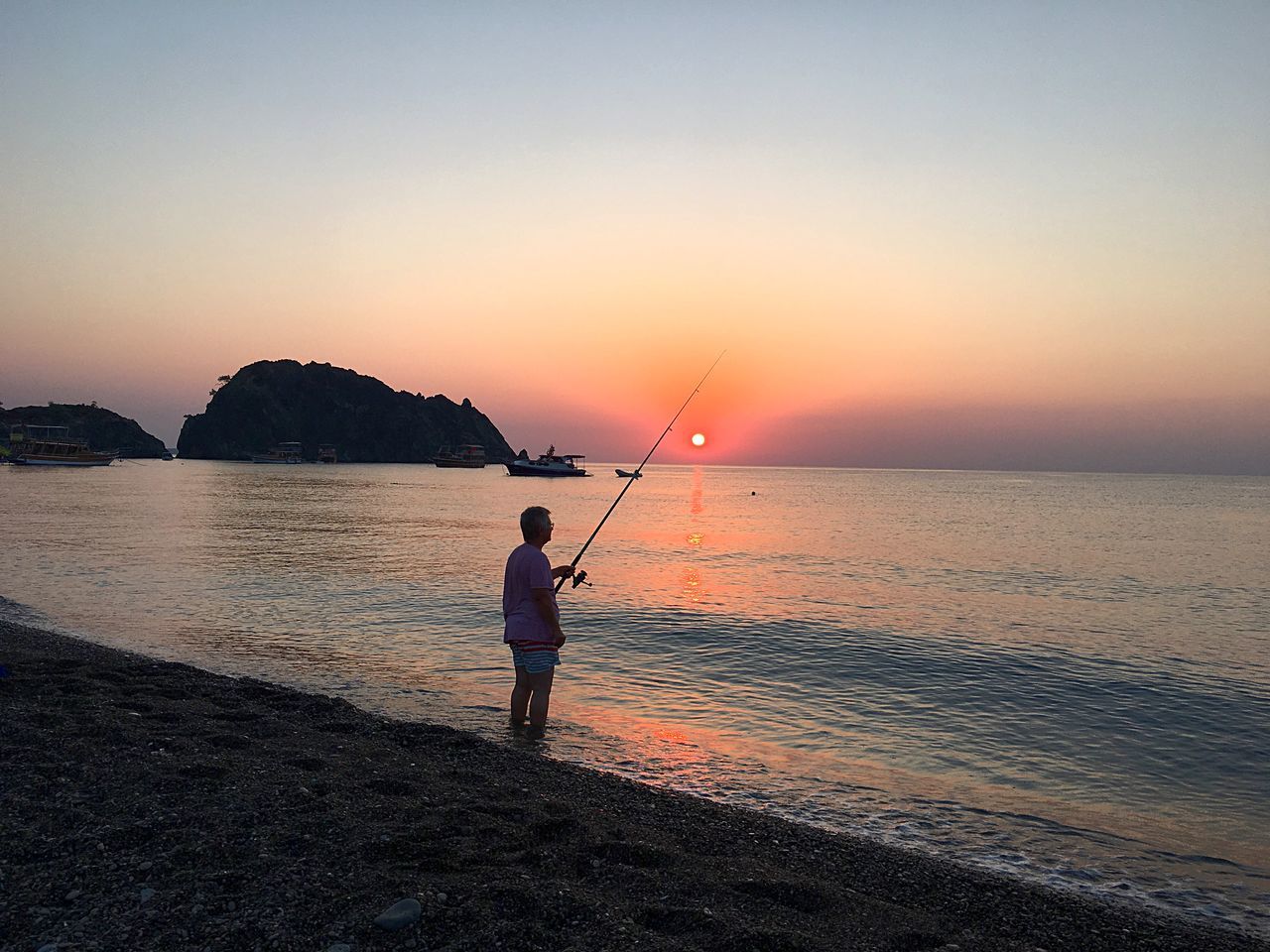 sunset, sea, full length, fishing, water, tranquil scene, one person, standing, beauty in nature, horizon over water, real people, silhouette, scenics, nature, tranquility, idyllic, leisure activity, fishing pole, beach, rear view, weekend activities, sky, clear sky, outdoors, lifestyles, fishing tackle, day, adult, people