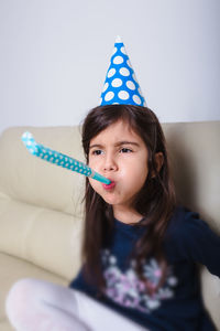 Cute girl blowing party horn blower while looking away at home
