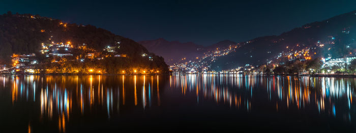 Illuminated city by lake against sky at night