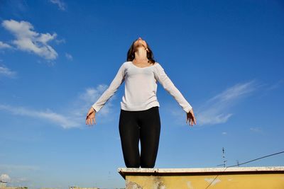 Low angle view of woman standing against blue sky