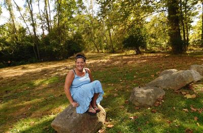 Portrait of smiling mature woman sitting on rock in forest