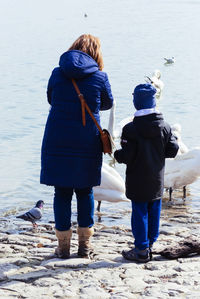 Rear view of woman with son standing by birds at lakeshore