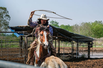 Man riding horse in ranch against clear sky