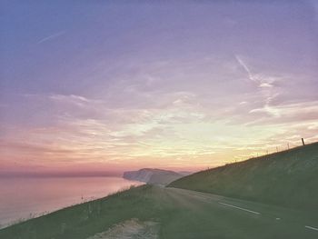 Road by sea against sky during sunset