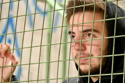 Portrait of young man looking through fence