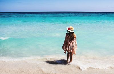 Rear view of young woman standing at beach against sky