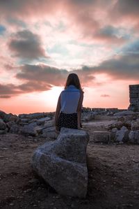 Rear view of woman standing on rock against sky during sunset