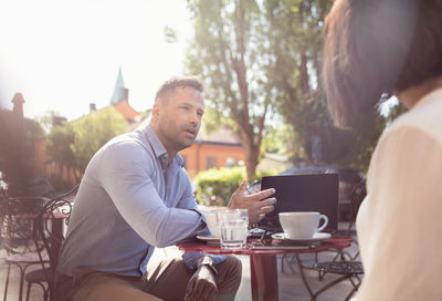 Businessman talking to female colleague at sidewalk cafe on sunny day