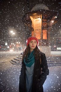 Portrait of young woman standing against illuminated wall during winter