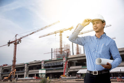 Confident architect with blueprint standing at construction site