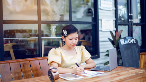 Young woman using phone while sitting on table