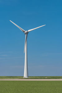 Windmill on land against clear blue sky