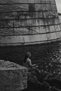Side view of woman sitting on rock against lake