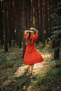 Alone woman in red dress dance on sun pine forest nature background