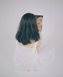 Rear view of woman looking in mirror against white background