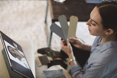 High angle view of female entrepreneur holding labels while talking to colleague on video conference at home office