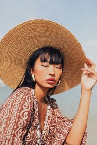 Young woman wearing hat sitting at beach against sky