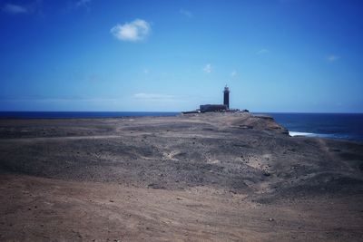 Lighthouse on beach by sea against sky