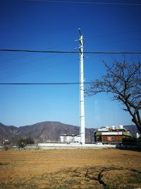 Electricity pylon by mountains against clear blue sky