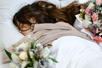 Girl sleeps on a white pillow . bouquets of flowers stand around it. she is wearing pajamas