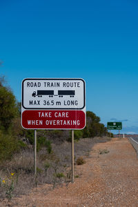 Information sign by road against clear blue sky