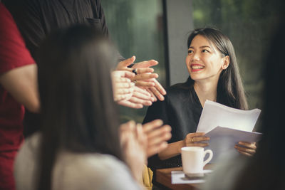 Woman holding papers by colleagues applauding