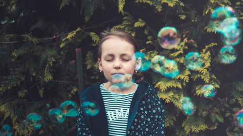 Girl with closed eyes standing amidst bubbles against plants