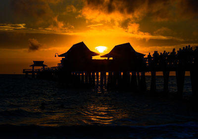 Silhouette built structure on beach against orange sky