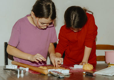 Two girls bake cookies, removing excess dough.