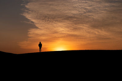 Silhouette person standing on land against sky during sunset