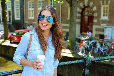 Young woman wearing sunglasses and holding disposable cup of coffee