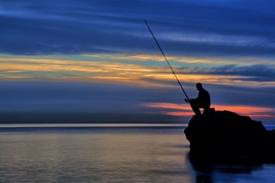 Silhouette man fishing in sea against sky during sunset