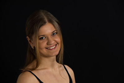 Portrait of smiling young woman against black background