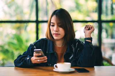 Woman using phone sitting by table in cafe