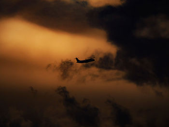 Low angle view of silhouette airplane flying against sky during sunset