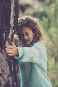 Young woman standing against tree trunk